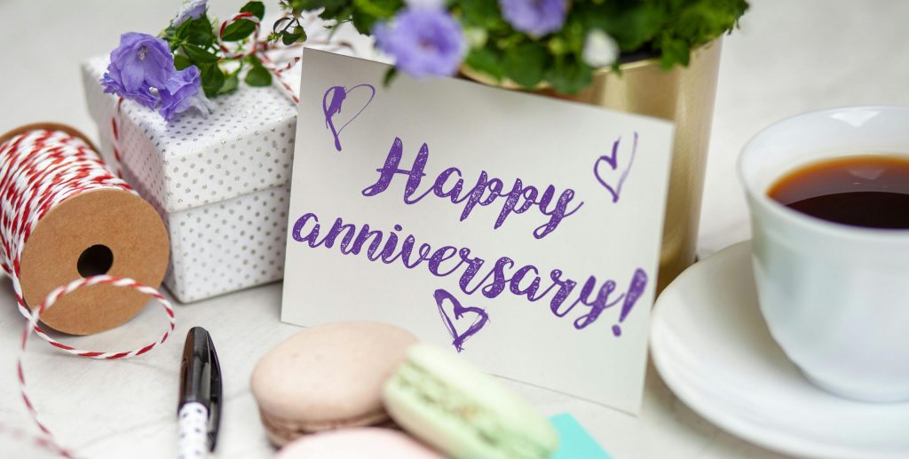 Happy anniversary card with flowers, gift, macarons, and coffee on a table.